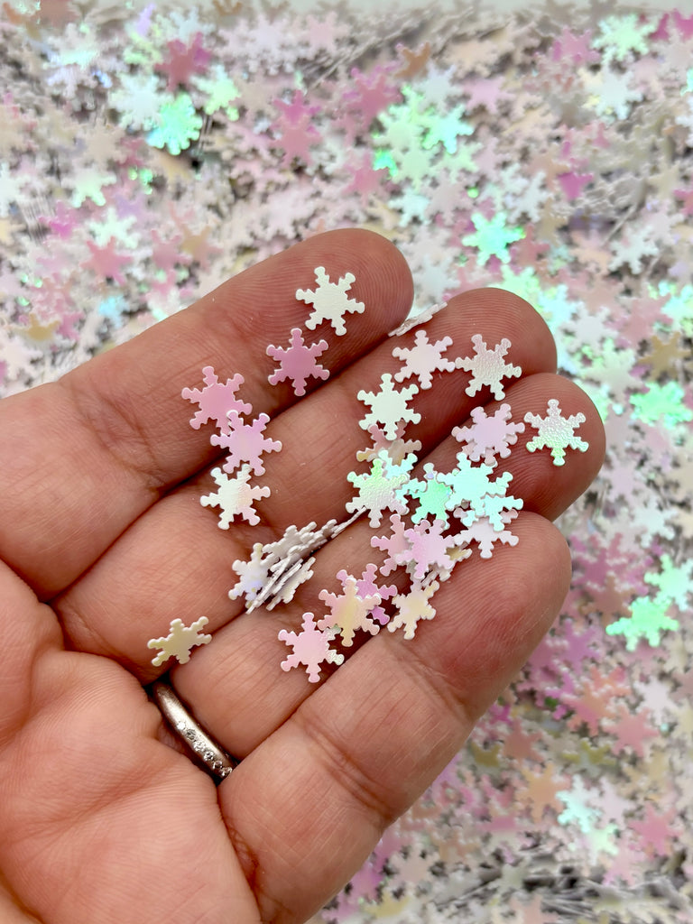 A hand holding a collection of small, white and pink glitter snowflakes against a background of more glitter snowflakes.