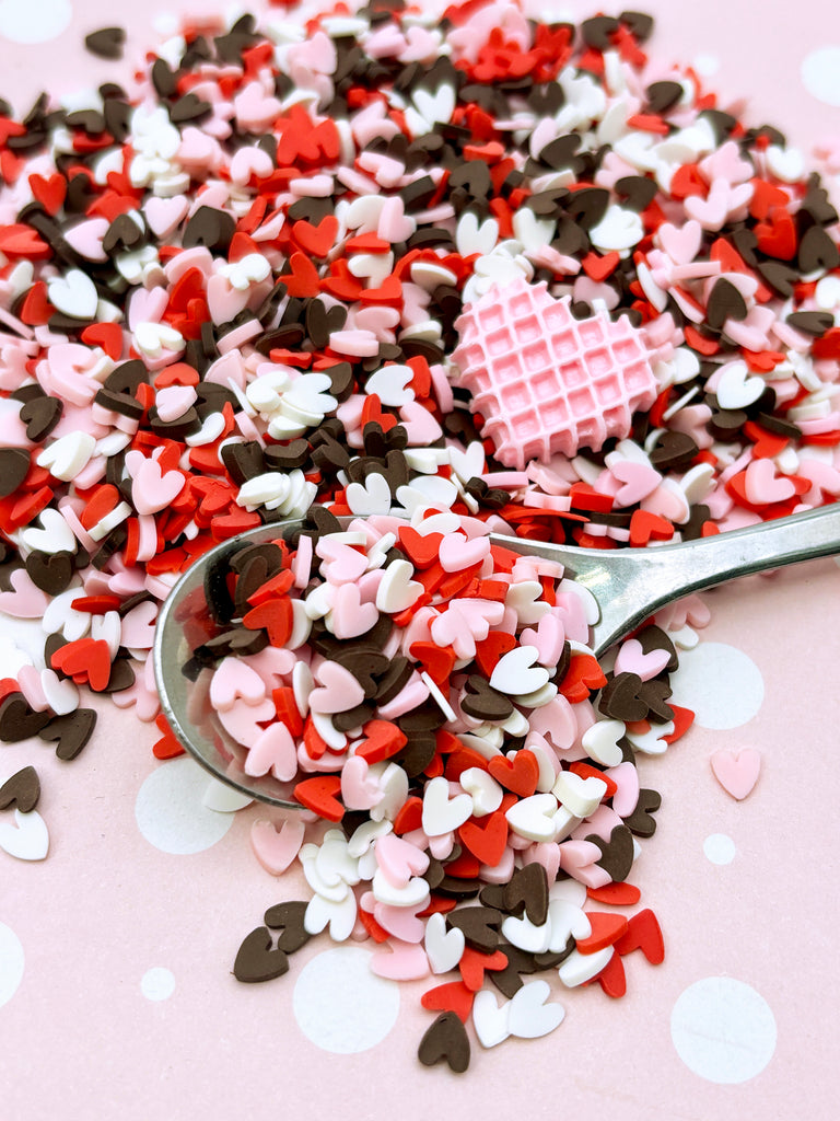 a spoon full of heart shaped sprinkles on a pink background