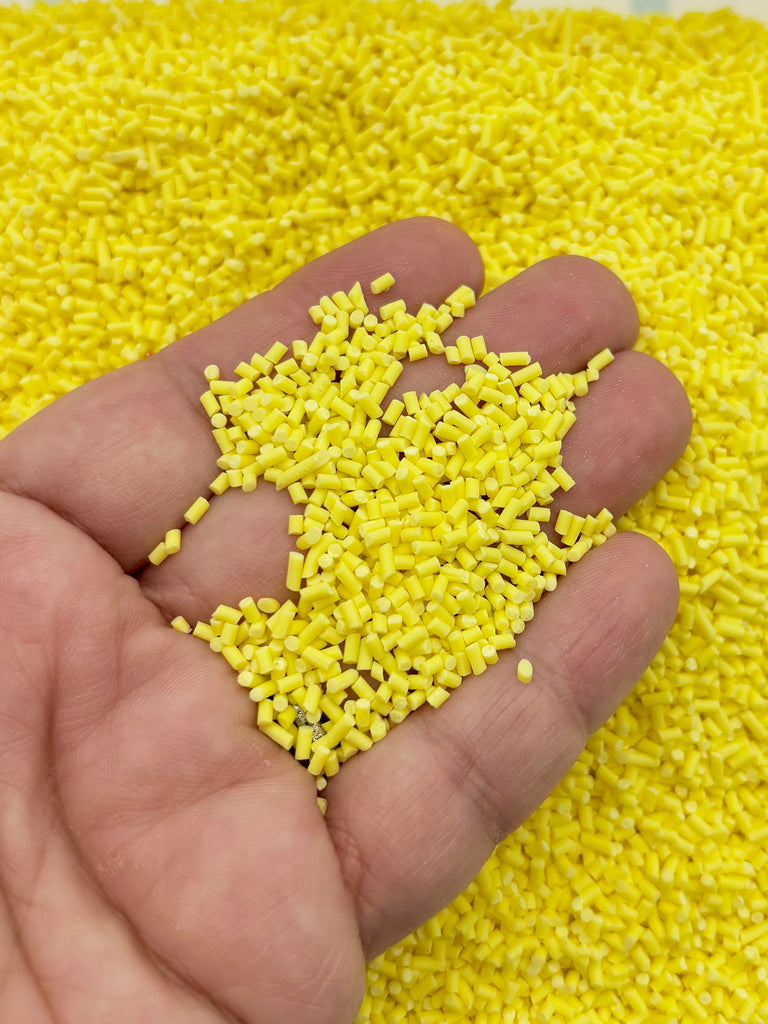 A hand is holding a pile of yellow plastic beads or grains, with the grains scattered around the palm of the hand.