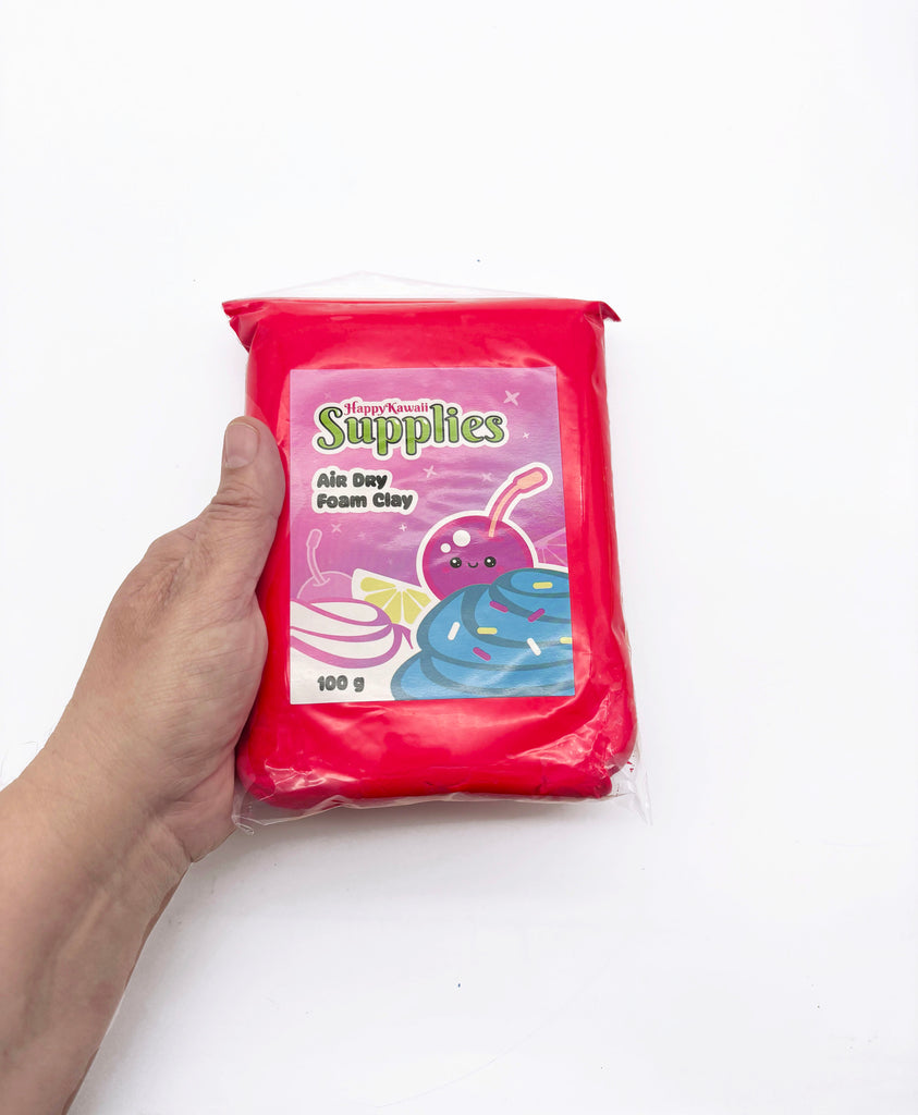 A hand is holding a red package of HappyKawaii Supplies' Air Day Foam Clay.