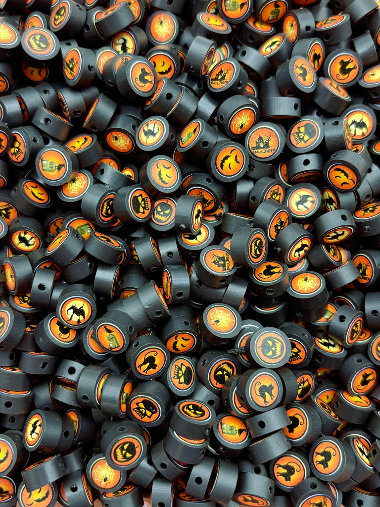 The image is a close-up of a pile of black beads with orange and black Halloween-themed designs, including bats, pumpkins, and other spooky symbols.