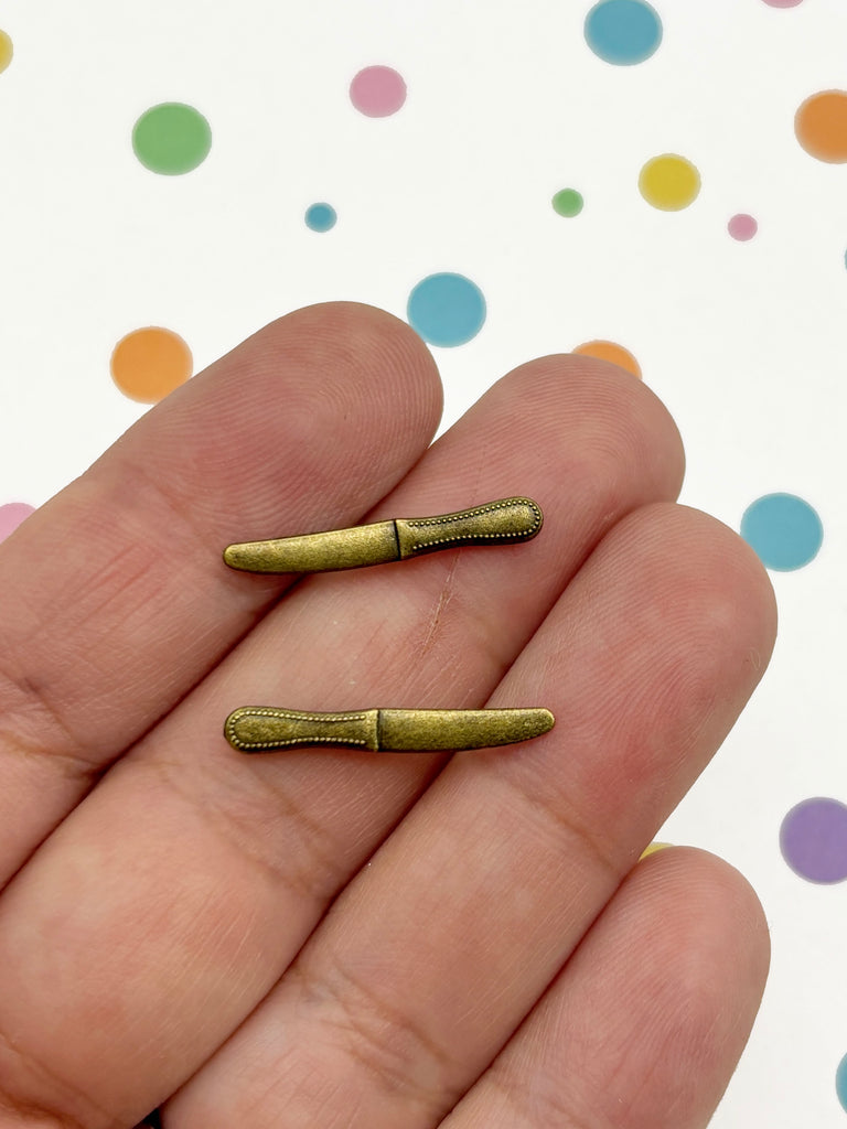 A hand holding two small, gold-colored knives against a background with colorful polka dots.