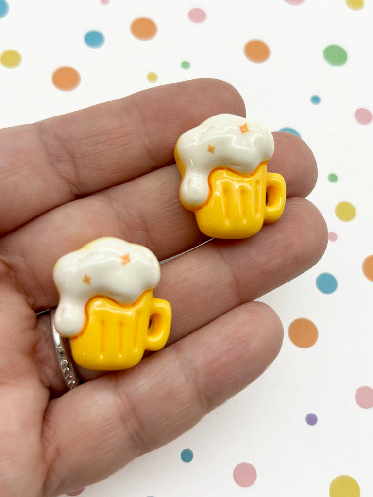 A hand holding two yellow foam-topped beer mug-shaped charms against a background with colorful polka dots.