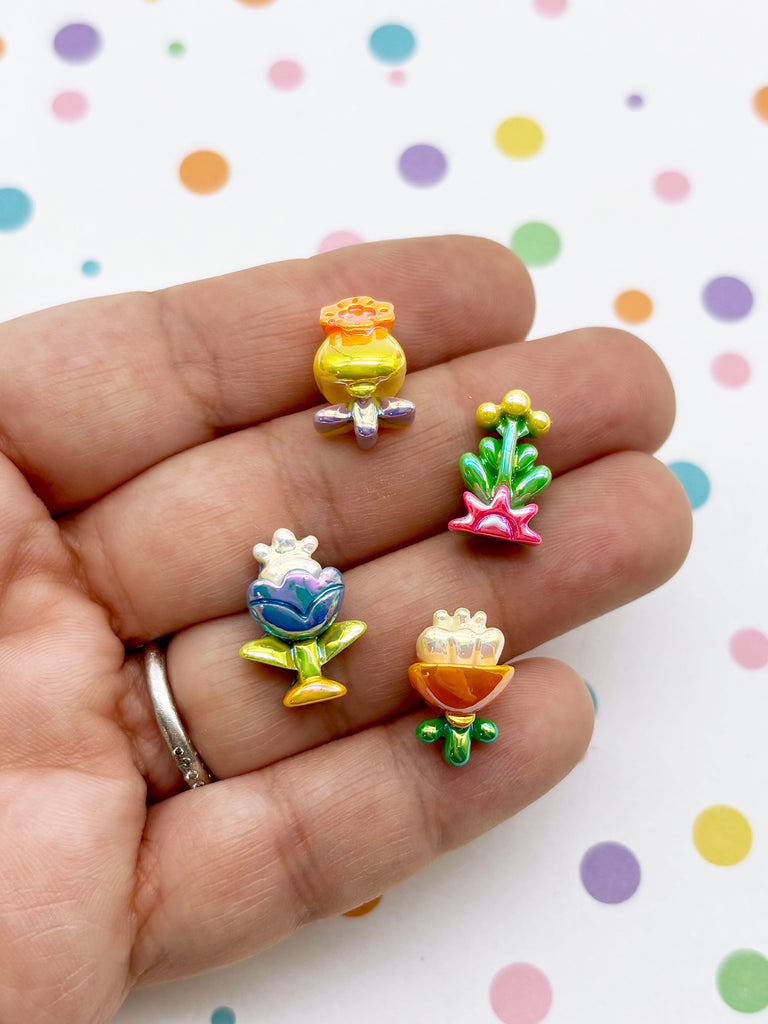 A hand holding four small, colorful plastic flower ornaments against a background with polka dots.