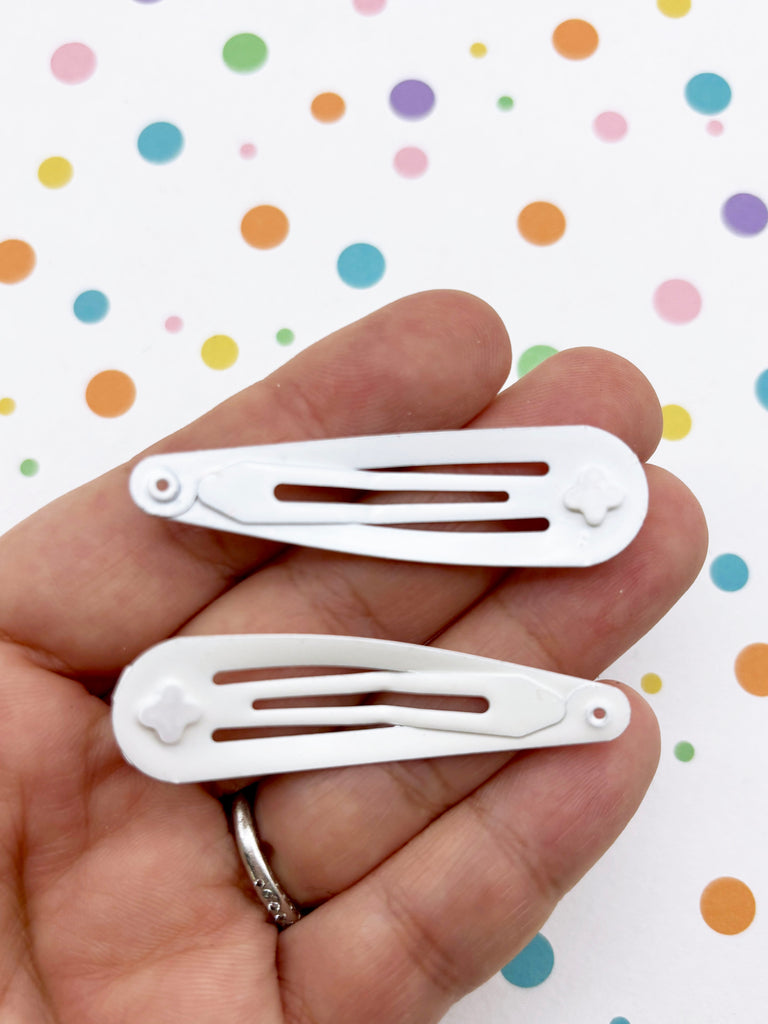 A hand holding two white hair clips against a background with colorful polka dots.