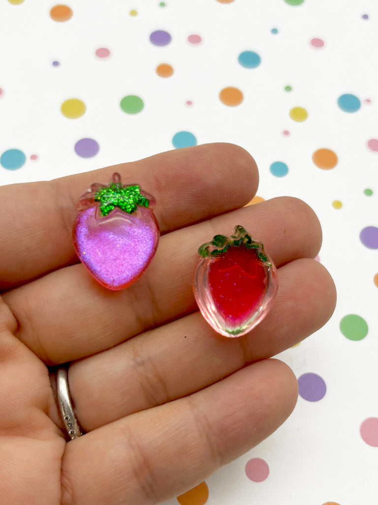 a hand holding two small strawberry shaped earrings