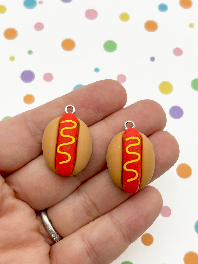 A hand holding two small hot dog charms against a background with colorful polka dots.