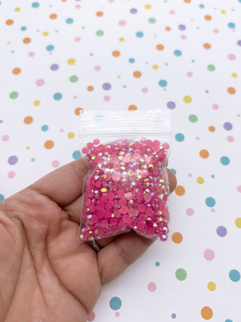 A hand is holding a small bag filled with pink glittery beads against a background with colorful polka dots.