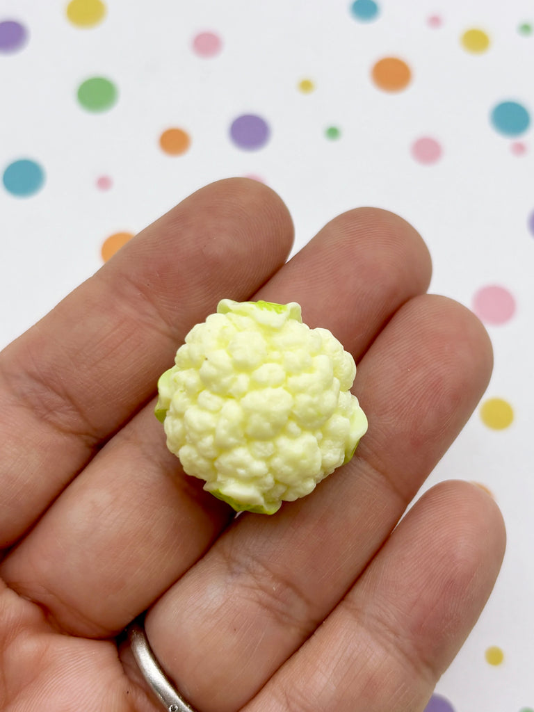 A hand holding a small, yellow cauliflower in front of a background with colorful polka dots.