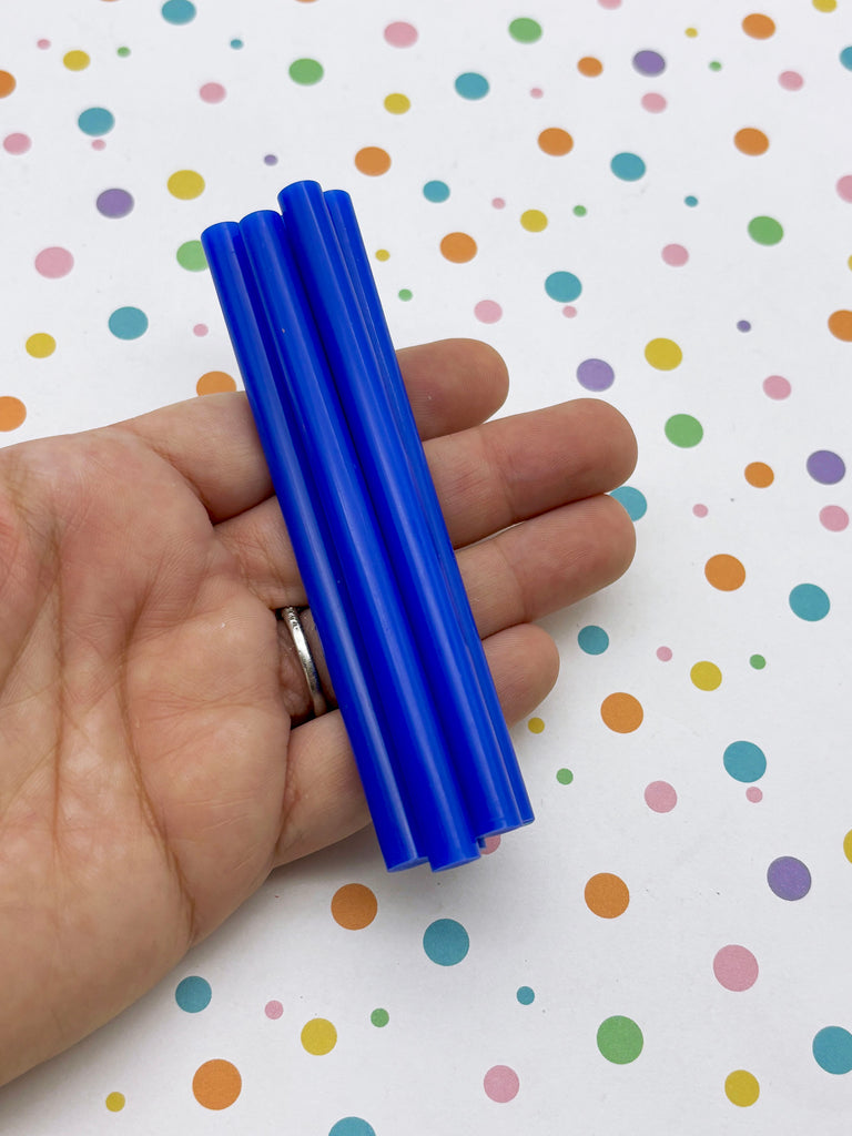 A hand holding a set of blue plastic straws against a background with colorful polka dots.