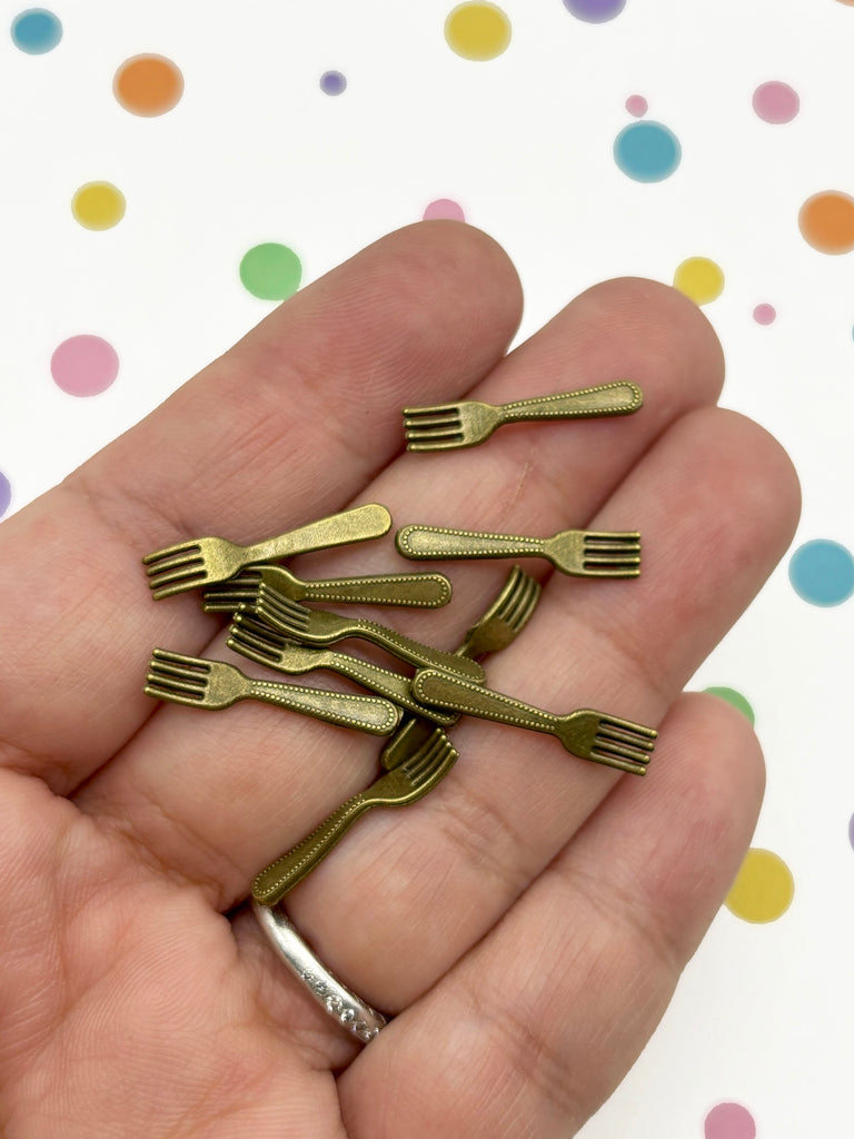 A hand holding a collection of small, gold-colored metal forks against a background with colorful polka dots.