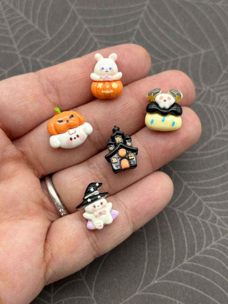 A hand holding a collection of small, colorful plastic figurines, including a pumpkin, a house, a witch, and other Halloween-themed characters.
