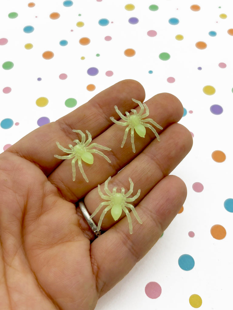 a hand holding two tiny yellow spider figurines