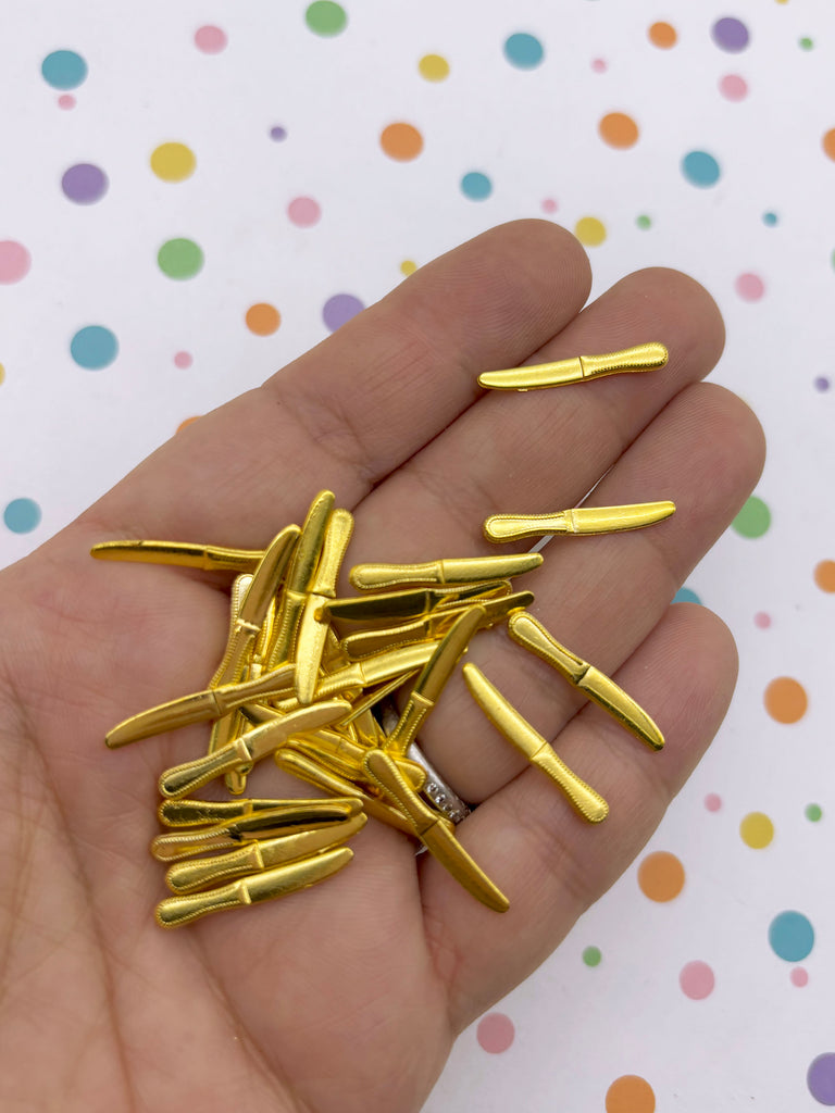A hand holding a pile of small, shiny gold-colored knife-shaped objects.