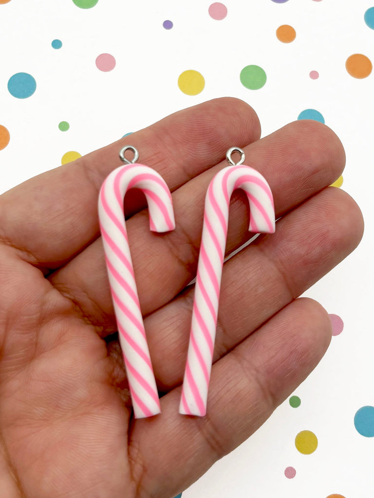 A hand holding two pink and white striped candy canes against a background with colorful polka dots.