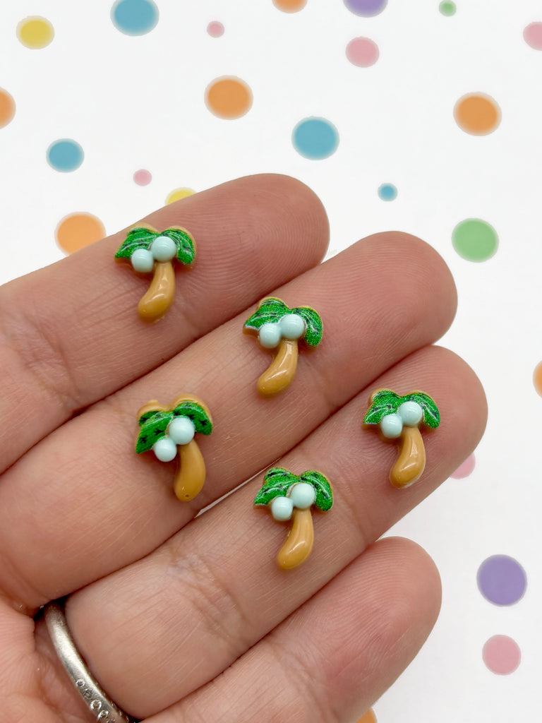 A hand holding five small, colorful beads shaped like bananas with green leaves on top, against a background with multicolored polka dots.