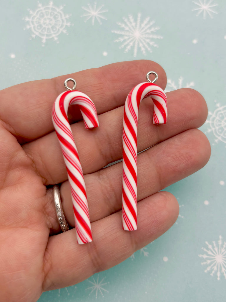 A hand holding two red and white striped candy canes against a snowy background.