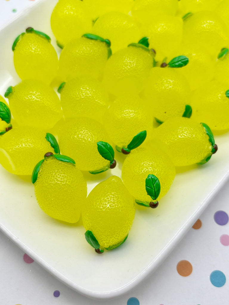 A white plate filled with yellow, lemon-shaped candies, each with a green leaf on top, arranged in a visually appealing manner.