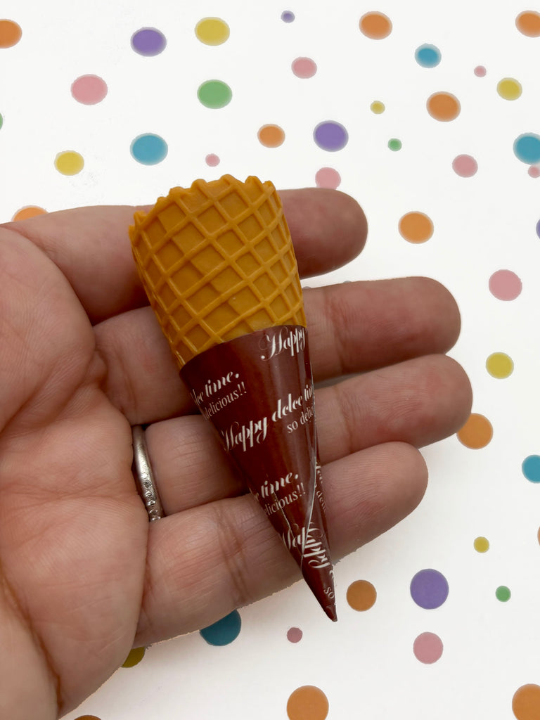 A hand holding a small cone-shaped object with a waffle-like texture and a brown color.