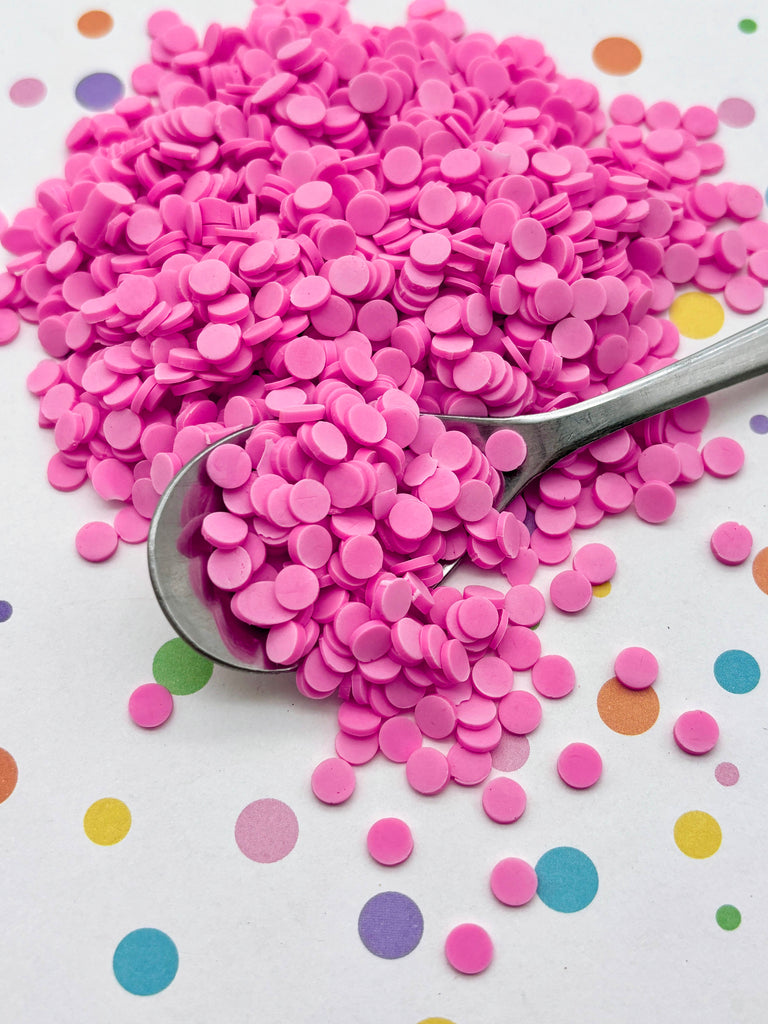 a pile of pink confetti-like objects on a white background, with a spoon partially submerged in the pile.