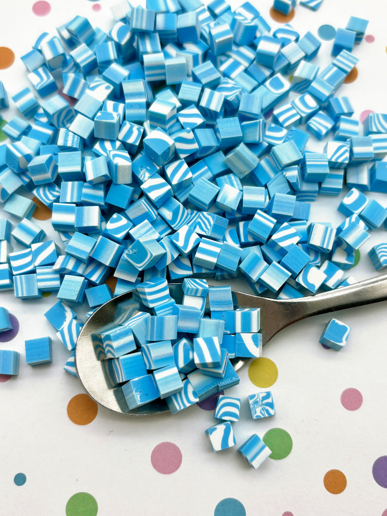 a spoon full of blue and white cubes next to a polka dot table cloth