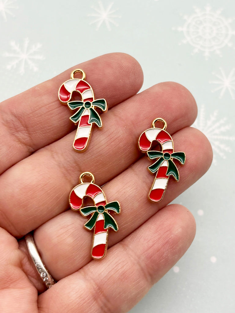 A hand holding three small, colorful candy cane charms against a snowy background.
