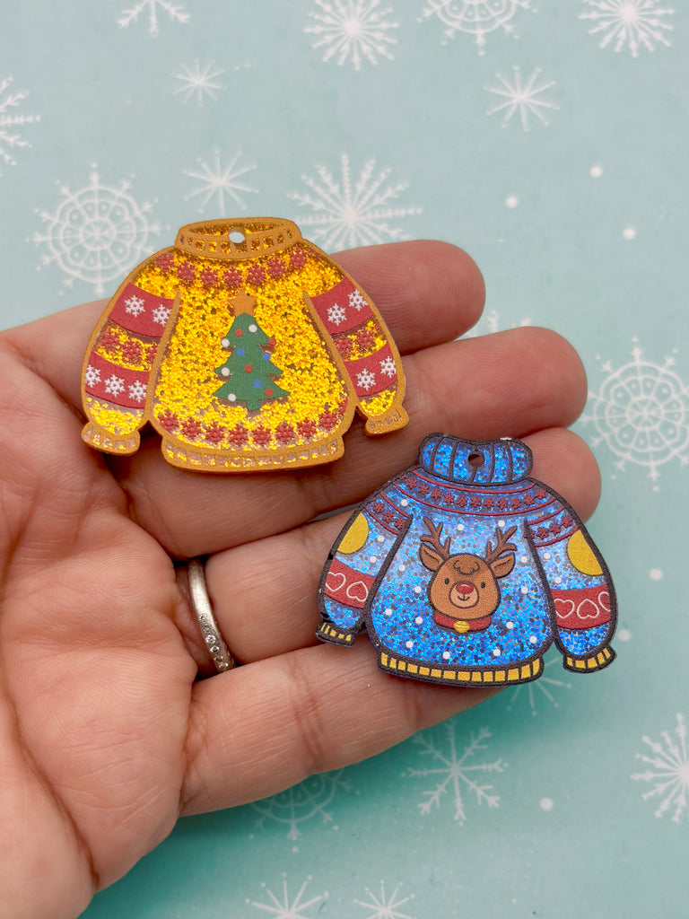 A hand holding two colorful Christmas-themed ornaments against a snowy background.