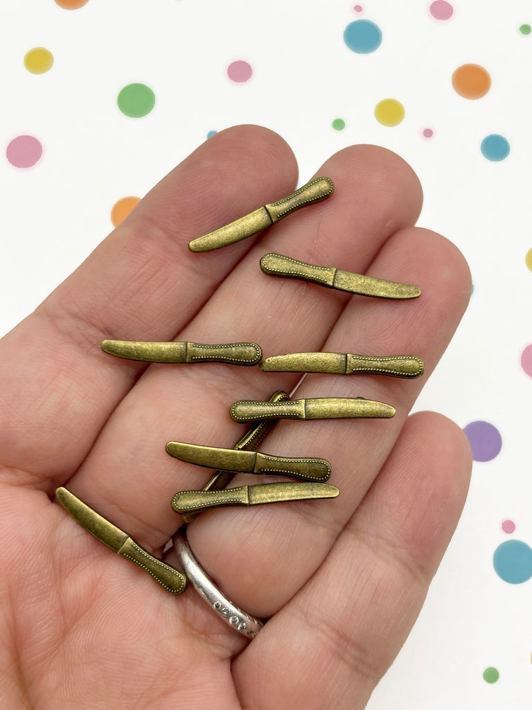 A hand holding a collection of small, brass-colored knife clips against a background with colorful polka dots.