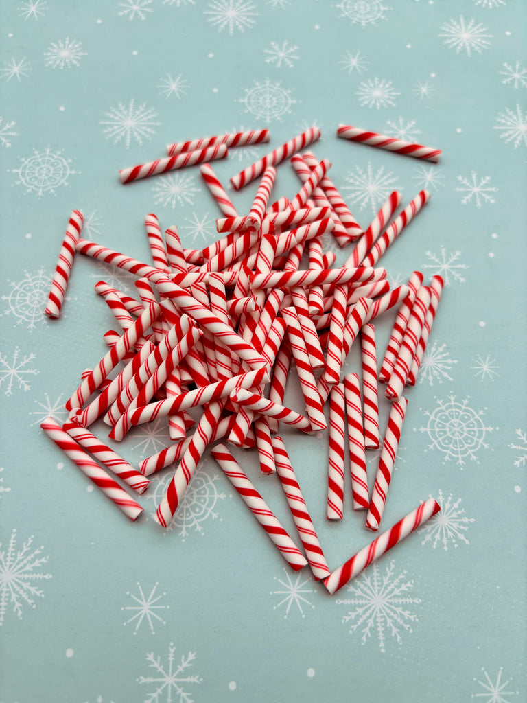 A pile of red and white striped candy canes is scattered on a light blue background with white snowflakes.