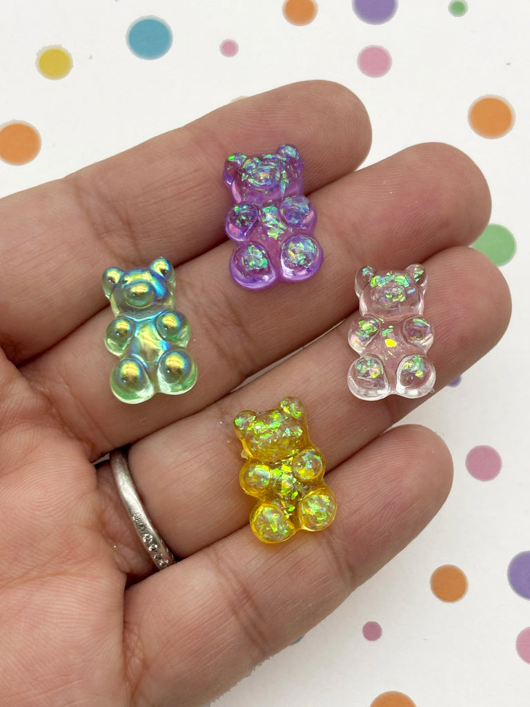 A hand holding four colorful gummy bear charms against a background with polka dots.