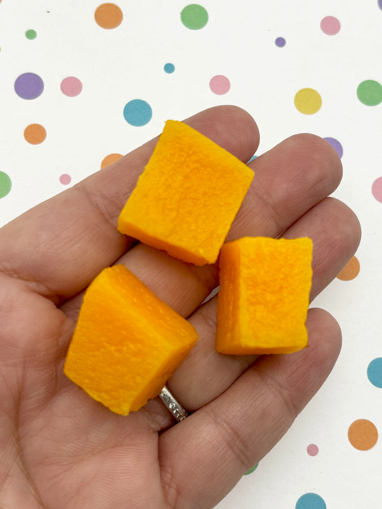 A hand holding three yellow cubes against a background with colorful polka dots.