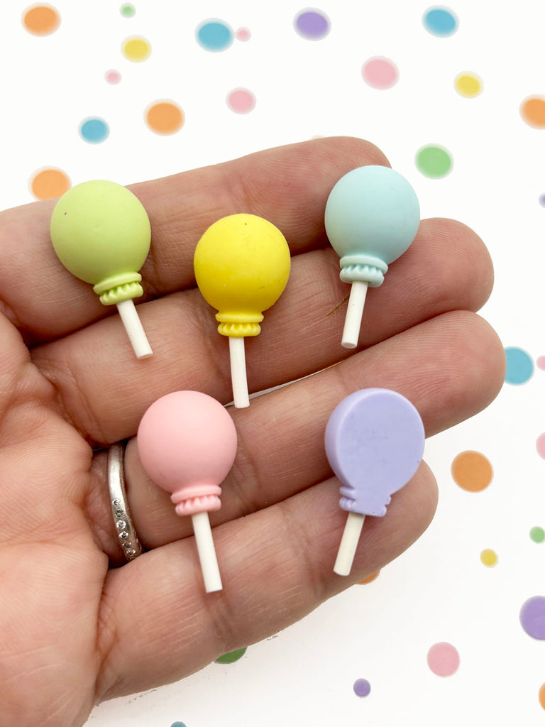 A hand holding five colorful lollipops against a background with polka dots.
