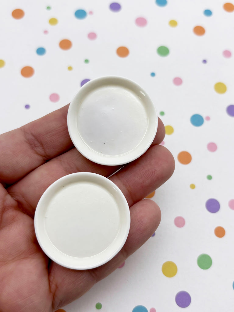 A hand holding two small white plates against a background with colorful polka dots.
