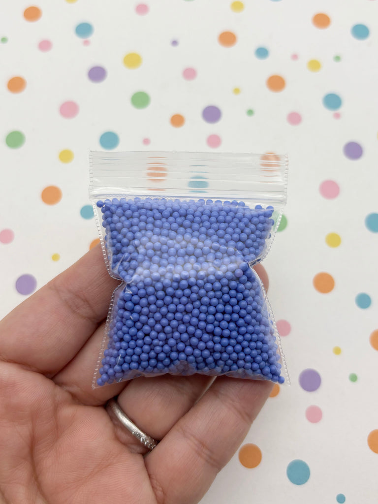 A hand holding a small bag filled with small, round blue beads against a background with colorful polka dots.