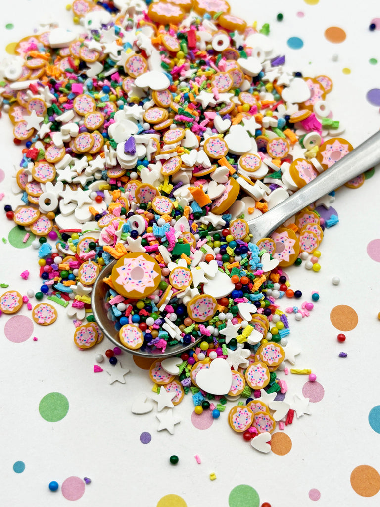 a pile of colorful sprinkles, including various shapes and sizes, scattered on a white surface with a spoon.
