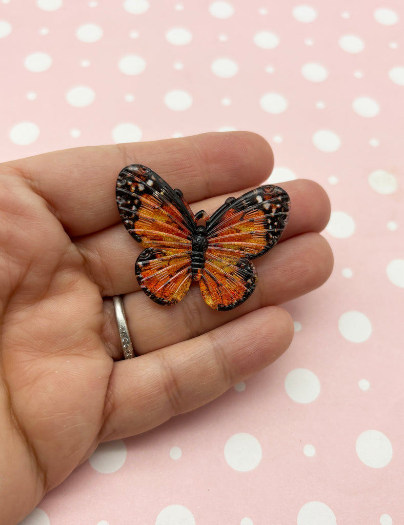 a hand holding a small orange butterfly on it's finger