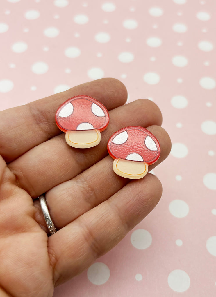 a hand holding a pair of mushroom shaped earrings