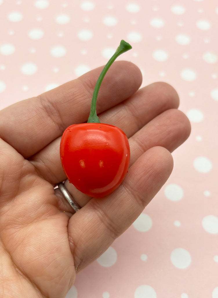 a hand holding a tiny cherry tomato on a pink background
