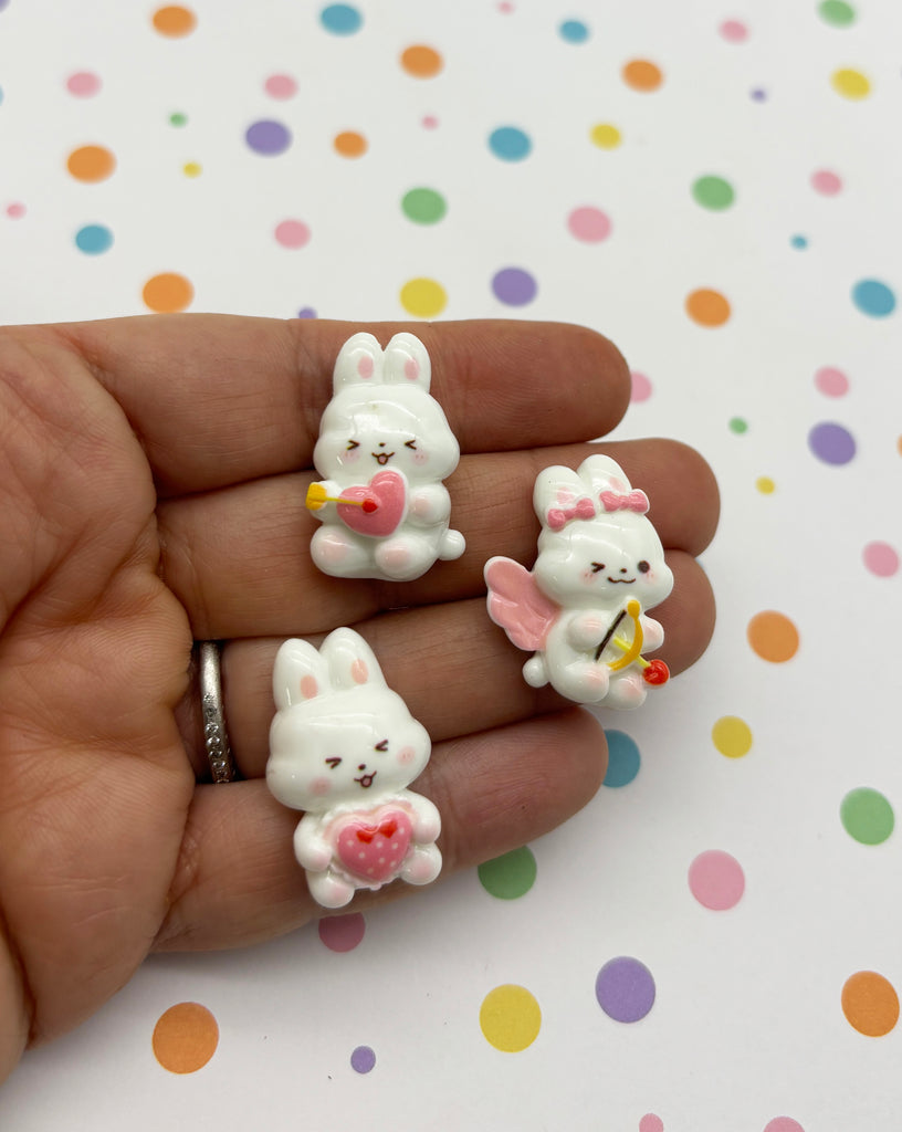 a hand holding three small white bunny figurines