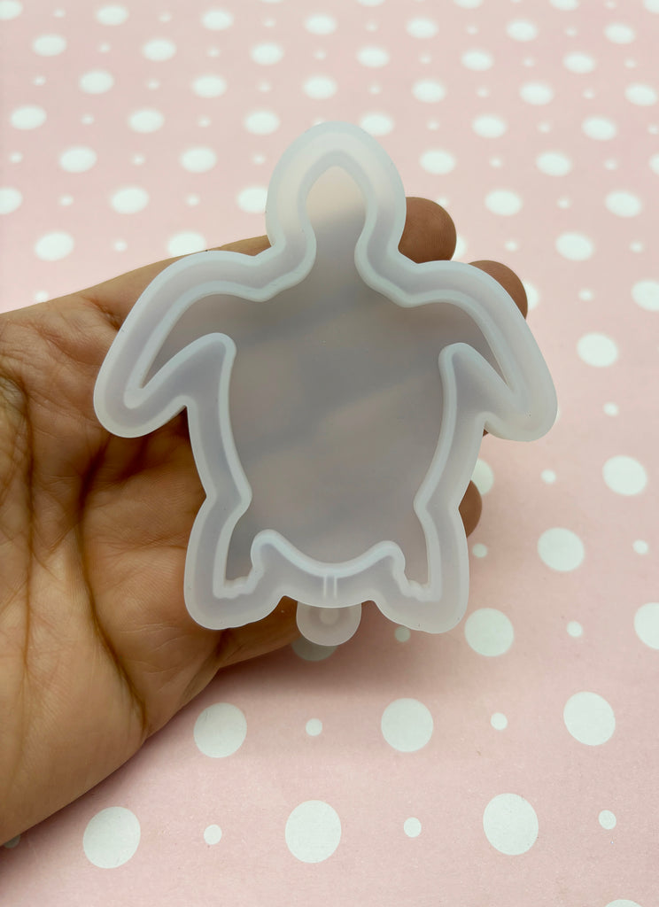 a hand holding a cookie cutter shaped like a turtle
