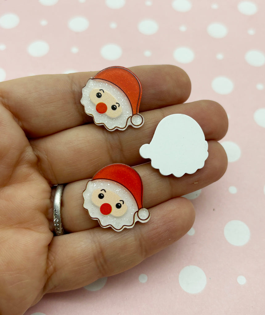a hand holding a pair of santa claus earrings