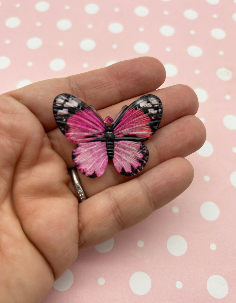 a hand holding a pink and black butterfly